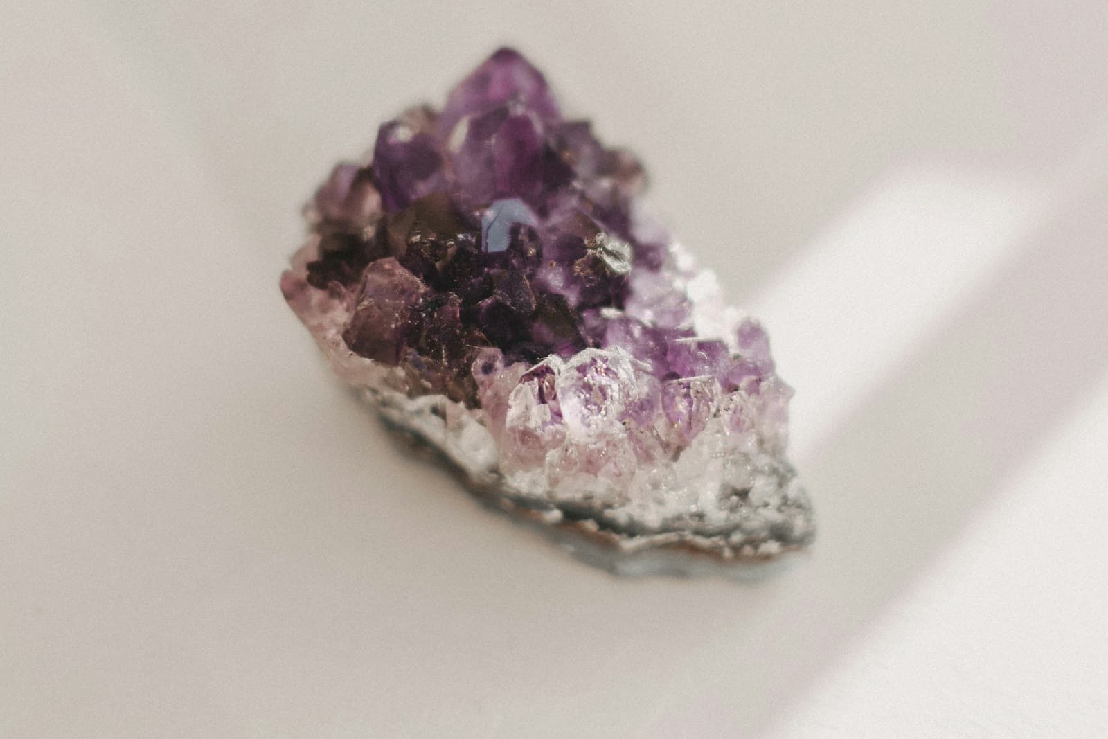A small raw amethyst cluster with purple crystal points on a pale cream surface in soft window light