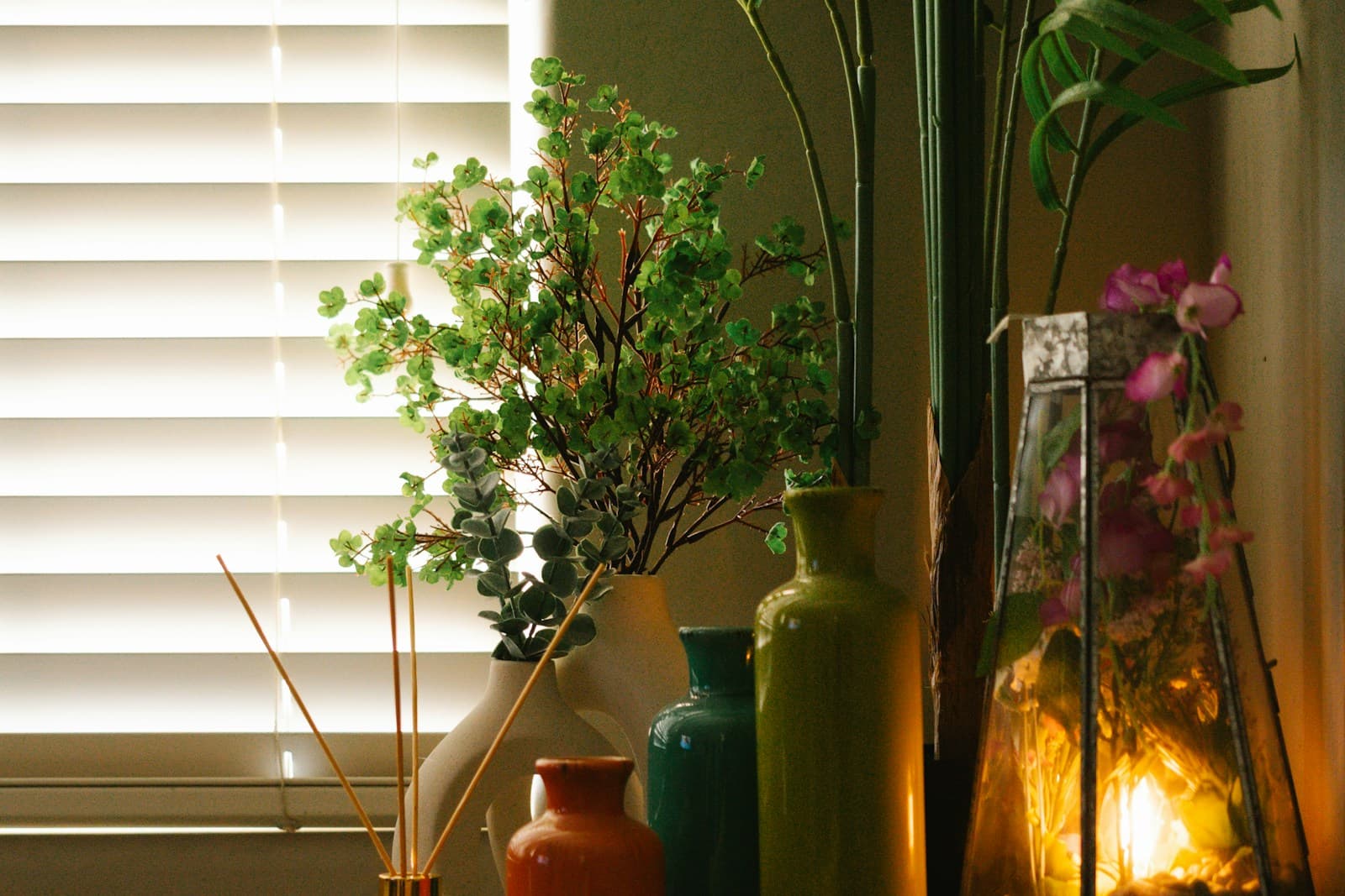 Warm windowsill with glass vases, a glowing lantern, and eucalyptus branches in evening light