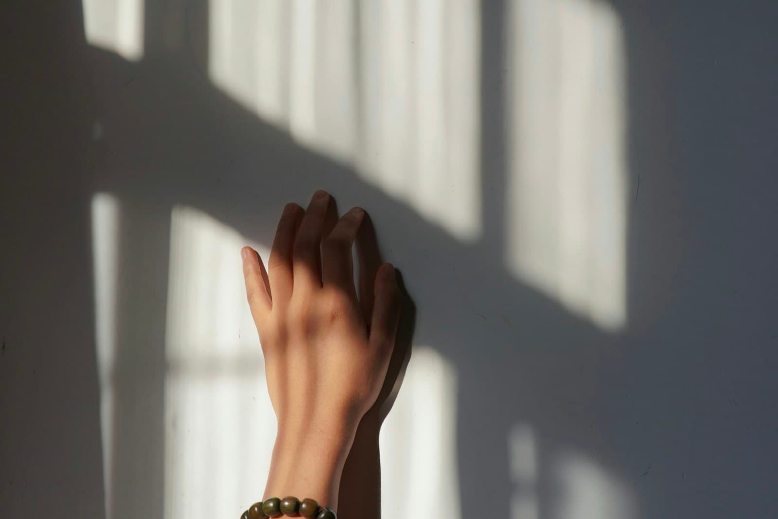 Hand reaching toward window light with a beaded bracelet visible at the wrist