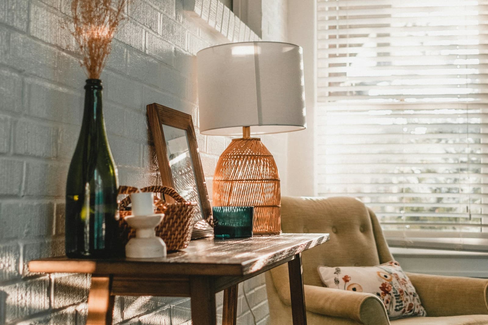 Warm console table vignette with dried grass, a woven lamp, and afternoon light through blinds